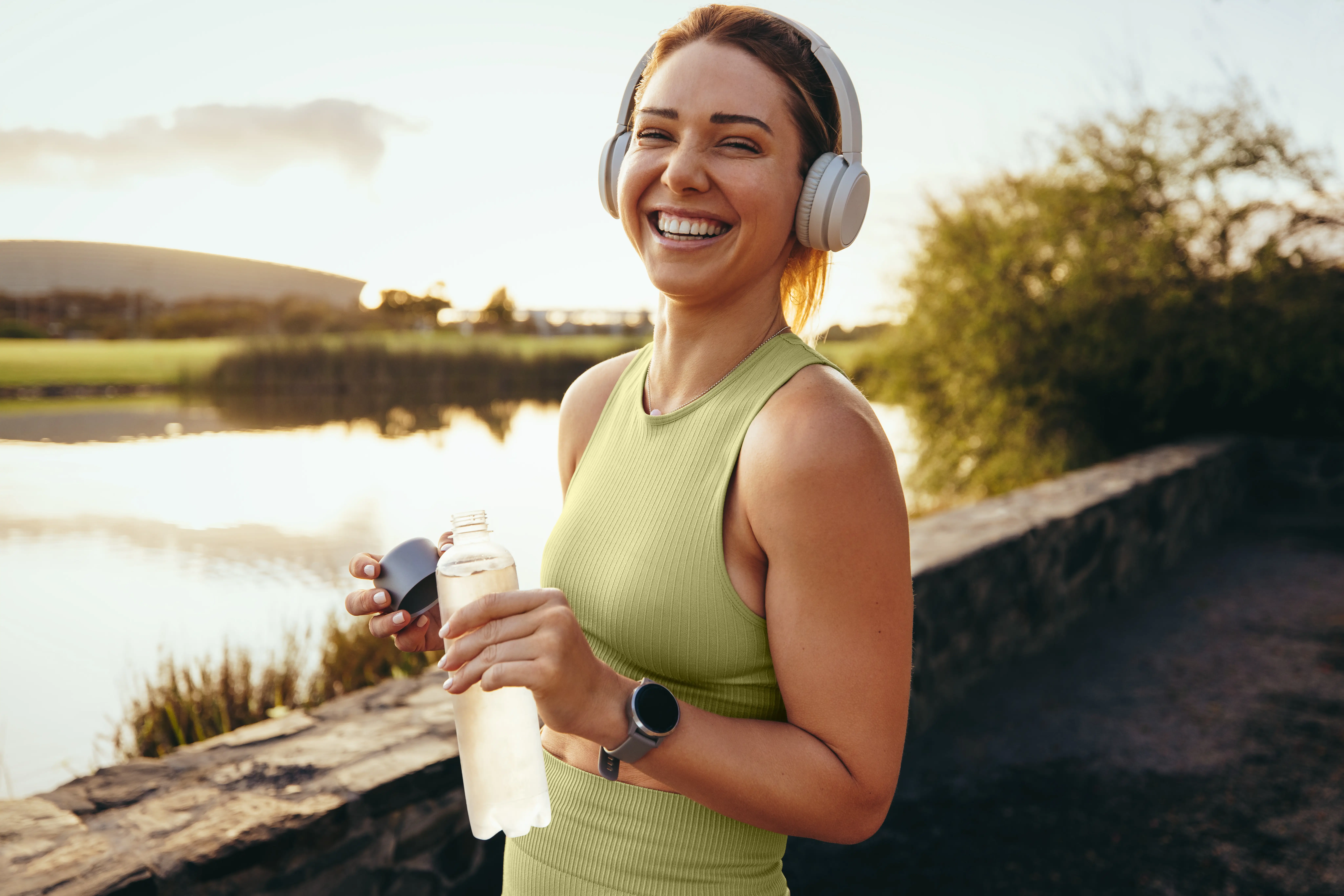 Woman wearing headphones holding a water bottle beside a lakeside path