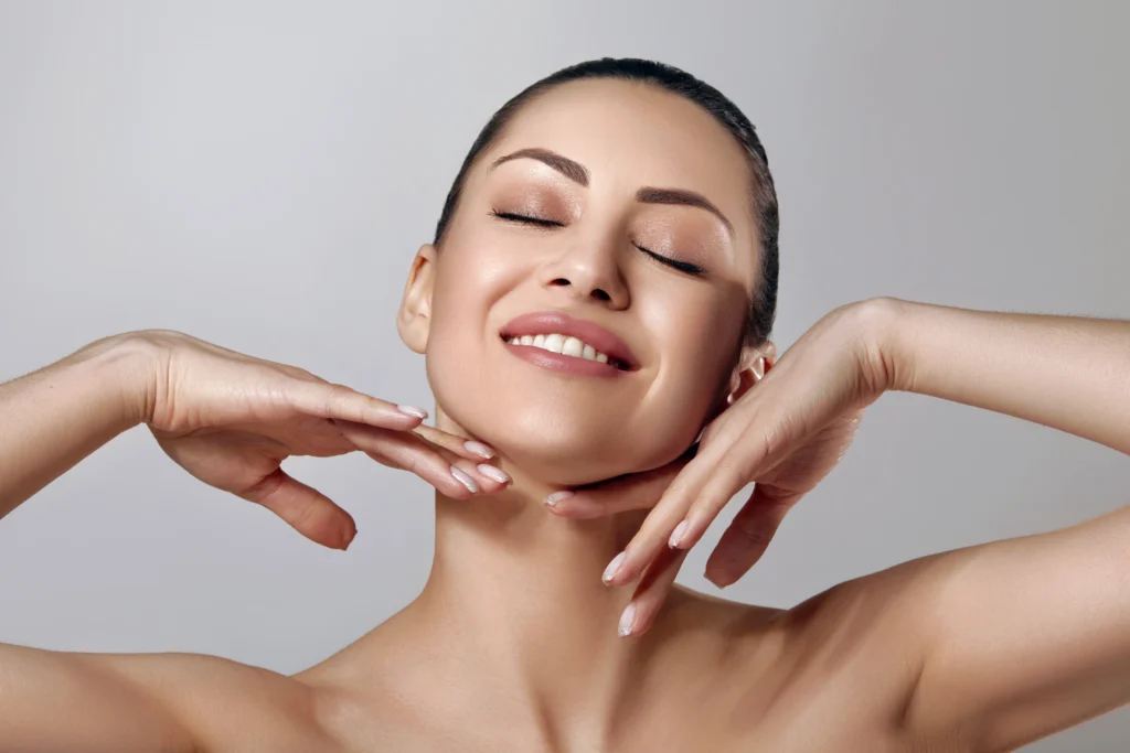 Person smiling with hands framing the jawline and cheeks against a neutral background