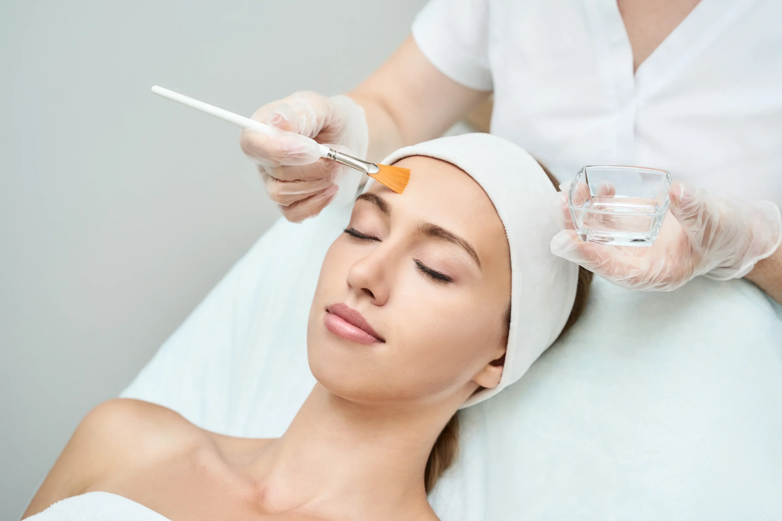 Practitioner applying a facial treatment to a client's forehead with a brush during a spa session