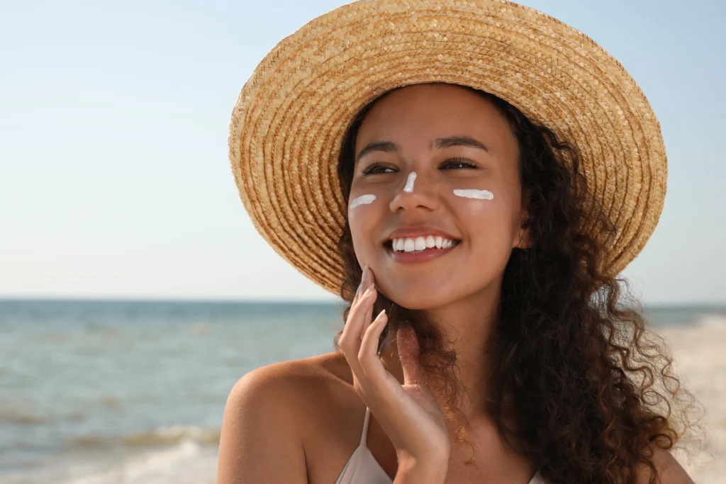Person wearing a wide-brim hat with sunscreen on the face while standing at the beach